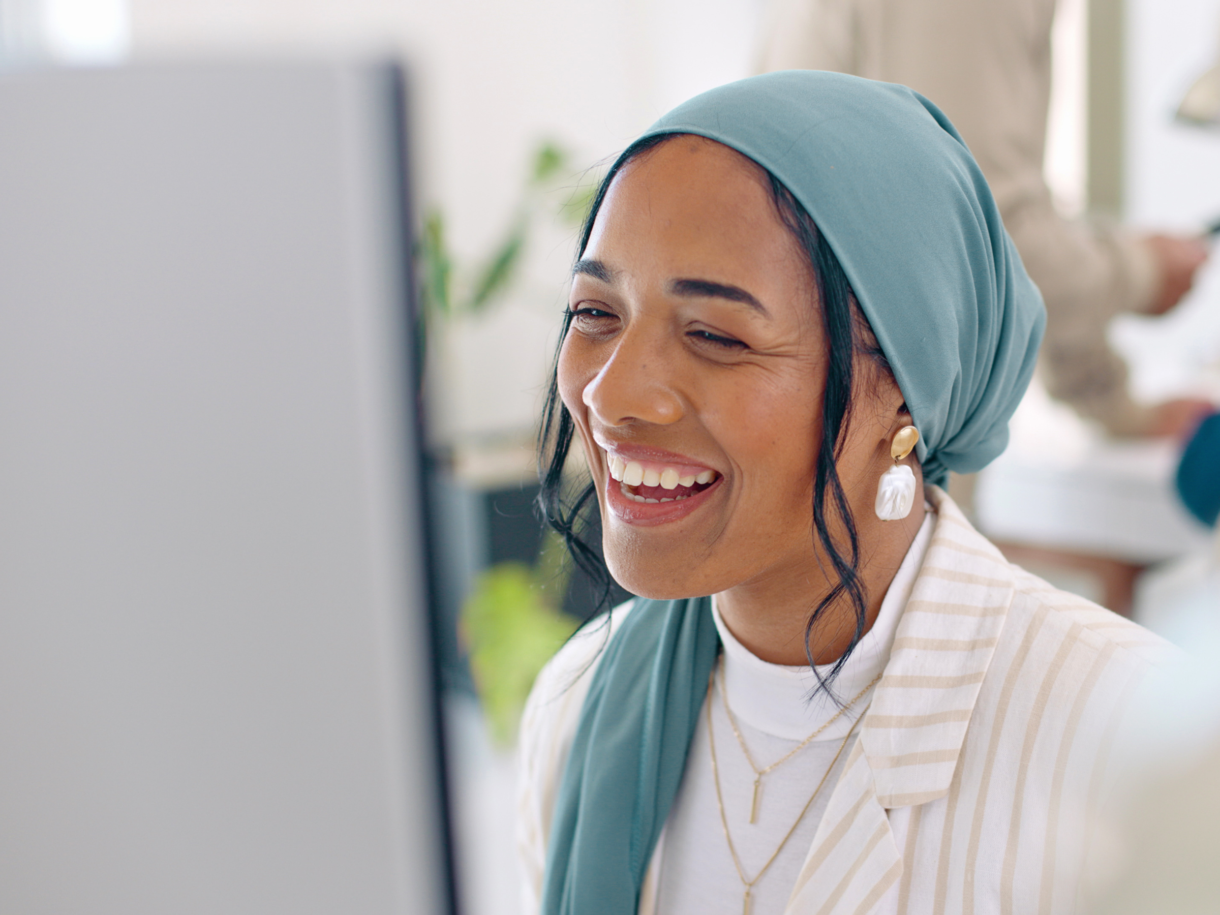 Woman in blue head wrap smiling at computer